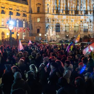 Demo zum Trans Day of Rememberance 2025 am Heldenplatz in Wien. Zu sehen ist eine Menschenmenge mit Flaggen und Schildern am Abend.