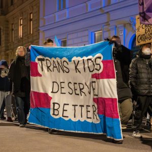 Demo zum Trans Day of Rememberance 2025 zu sehen ist der Demo-Zug und ganz groß eine Flagge von TNYV mit der Aufschrift "Trans Kids Deserve Better"