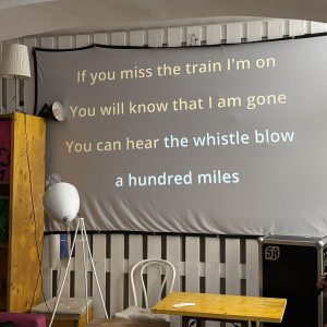 Canvas with karaoke texts in a room with yellow table, chairs and a speaker.