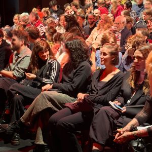 Publikum in einem Theater sitzt dicht gedrängt auf Reihenplätzen
